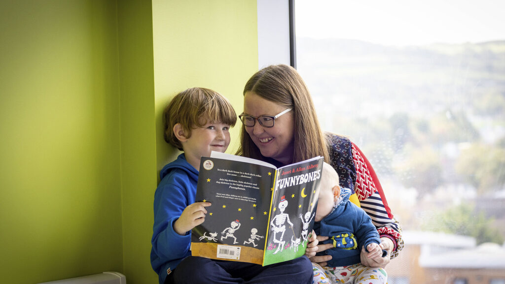 Child reading a book with mum and baby DPIL